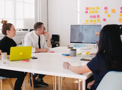 A diverse group of individuals gathered around a table, engrossed in their work on a laptop.