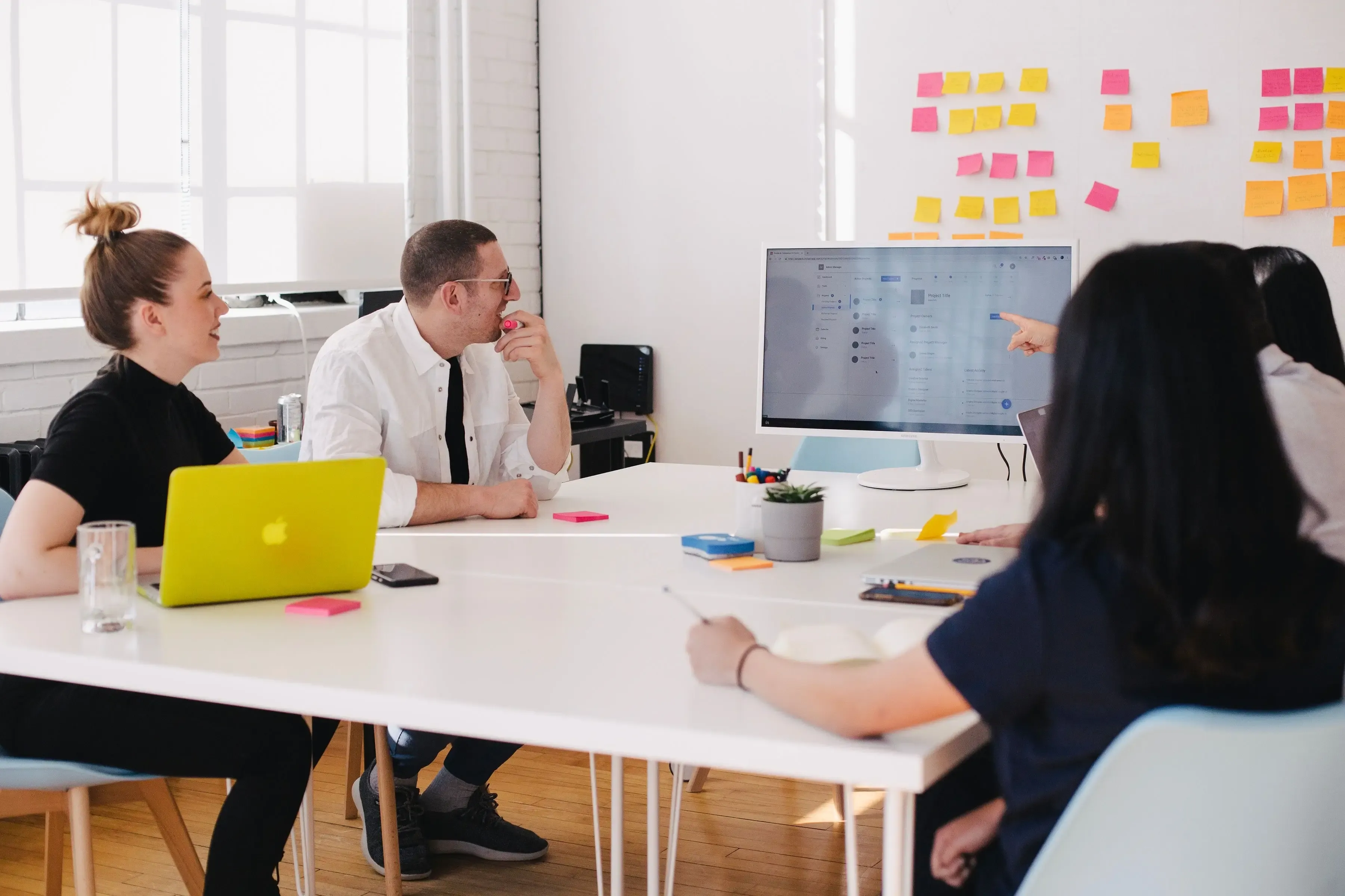 A diverse group of individuals gathered around a table, engrossed in their work on a laptop.