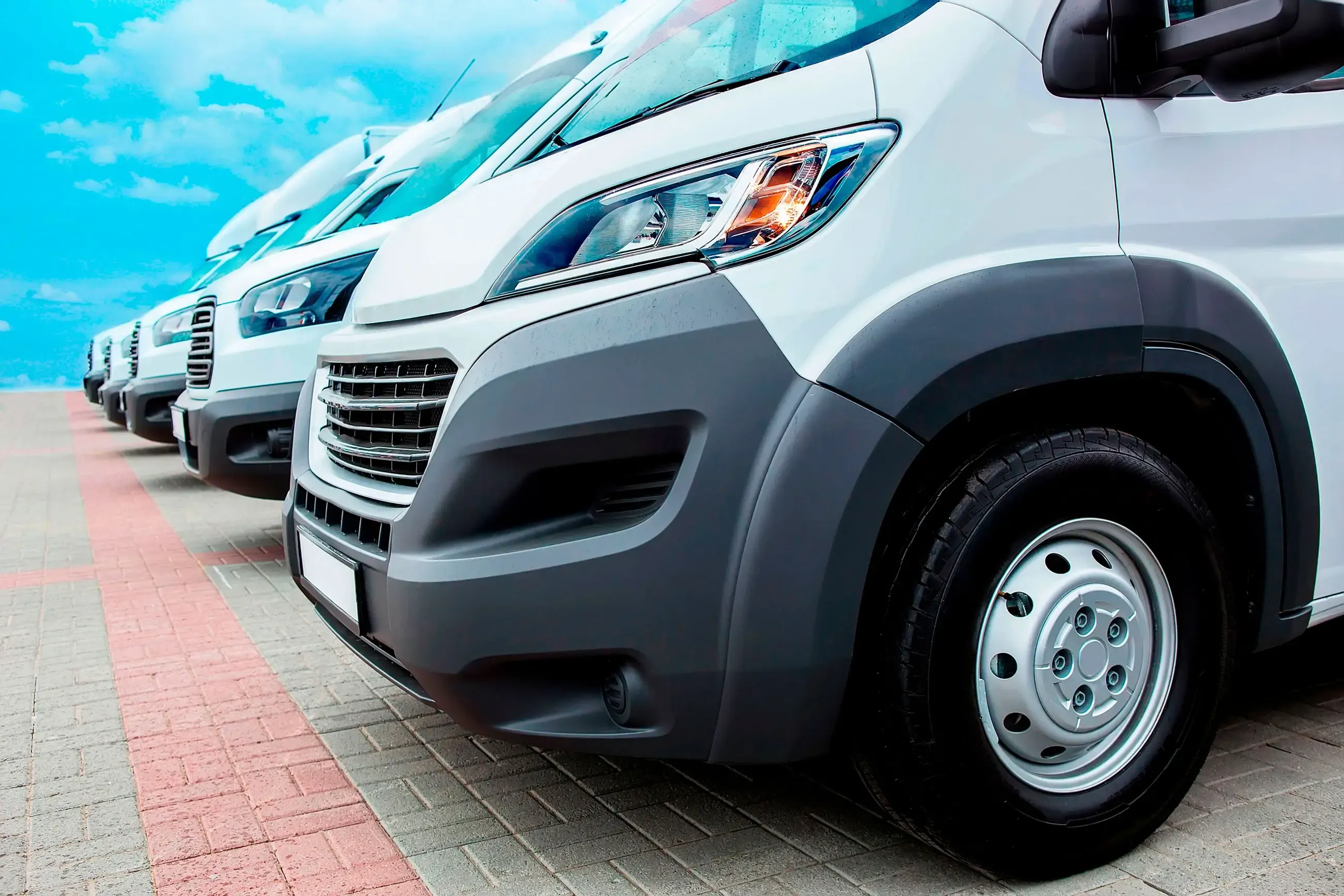 A line of white vans parked on a road, ready for transportation.