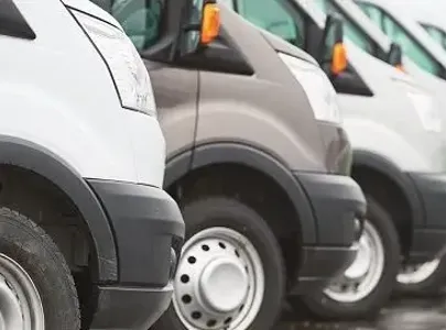 A lineup of white vans with only 1 being grey parked in a row.