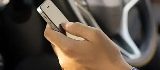 A person holding a cell phone whilst sitting in a car.