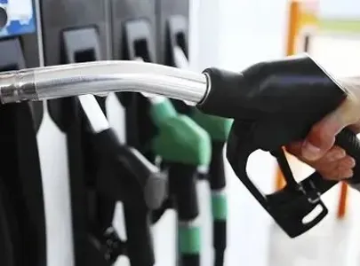 A person refuels their car at a gas station, holding the nozzle that they've picked up from the holder.